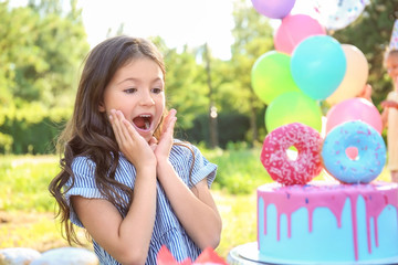 Emotional little girl with cake celebrating Birthday outdoors