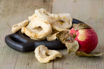   Dessert. Dried apple rings on a round wooden plate, next to a ripe apple on an old wooden table.
 