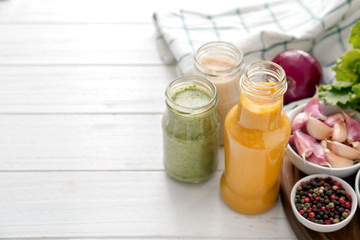Bottle and jars with different tasty sauces, spices, herbs and vegetables on white wooden table