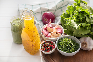 Bottle and jar with tasty sauces, spices, herbs and vegetables on white wooden table