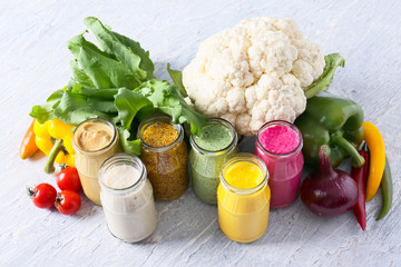 Jars with different tasty sauces and vegetables on light table