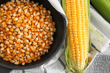 Frying pan with kernels and corn cob on wooden background