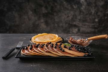 Delicious thin pancakes with berries and chocolate paste on dark table