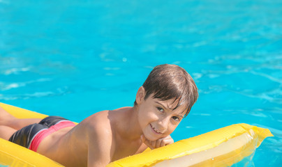 Cute boy on inflatable mattress in swimming pool on summer day