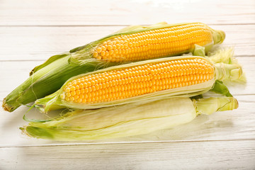 Fresh corn cobs on white wooden table
