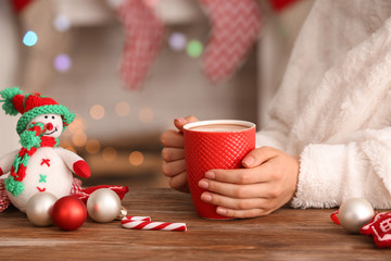 Woman with cup of delicious cocoa and Christmas decorations at table, closeup