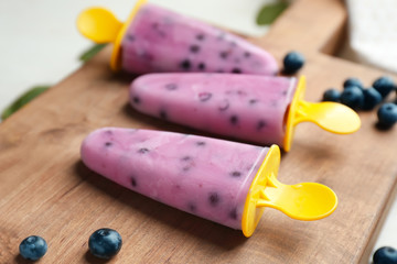 Tasty blueberry popsicles with berries on wooden board, closeup