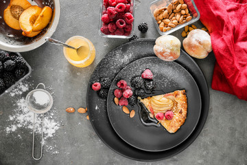 Plate with slice of delicious peach galette, honey and berries on dark table