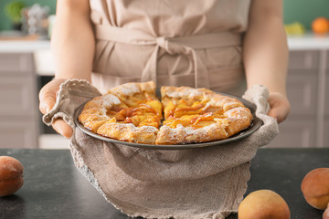 Woman with delicious peach galette in kitchen