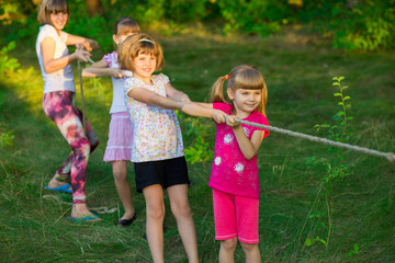 Group of happy children playing tug of war outside on grass. Kids pulling rope at park. Summer camp...