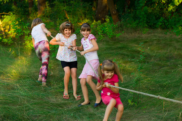 Fototapeta premium Group of happy children playing tug of war outside on grass. Kids pulling rope at park. Summer camp fun