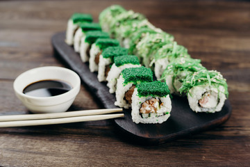 Japanese restaurant, sushi plate. Delicious seafood maki rolls on black wooden tray with sauce and chopsticks