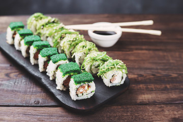 Japanese restaurant, sushi plate. Delicious seafood maki rolls on black wooden tray with sauce and chopsticks