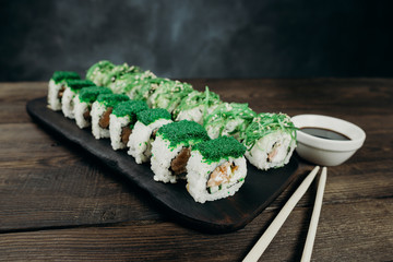 Japanese restaurant, sushi plate. Delicious seafood maki rolls on black wooden tray with sauce and chopsticks