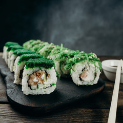 Japanese restaurant, sushi plate. Delicious seafood maki rolls on black wooden tray with sauce and chopsticks, copy space