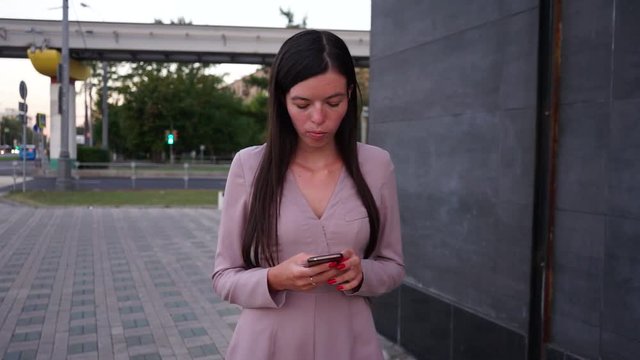 young girl in a pink dress uses smartphone and typing write message on phone city background MLS