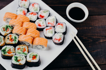 Japanese restaurant, sushi plate. Delicious seafood maki rolls on white plate with sauce and chopsticks