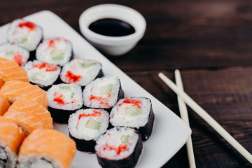 Japanese diet, seafood, property nutrition. Appetizing sushi rolls set on white plate with sauce and chopsticks