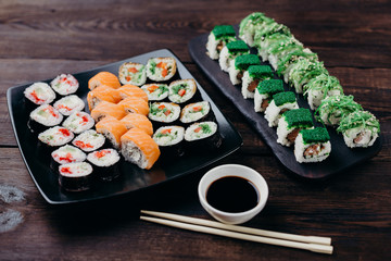Japanese restaurant menu photo, seafood, national cuisine. Delicious assortment of sushi. Appetizing rolls served on black plate with sauce and chopsticks