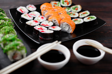 Japanese restaurant, sushi plate. Delicious seafood maki rolls on plate with sauce and chopsticks