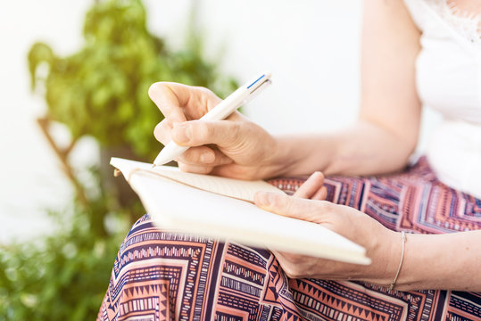 close-up of woman sitting on patio taking notes in notebook