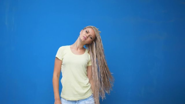 Trendy hipster girl shaking her braided hair pigtails and spinning around on blue background