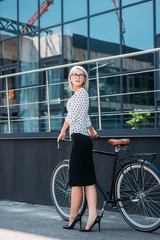 young businesswoman in stylish clothing with retro bicycle standing on street