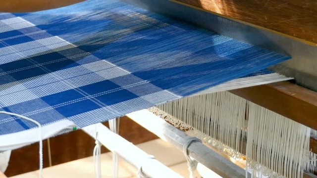 Close up woman is weaving Thai silk fabric by traditional weave machine in textile industry.