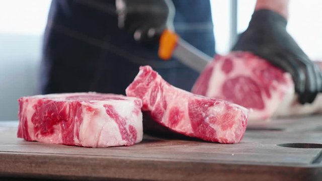 Chef cuts raw meat on the wood board with the knife, close-up