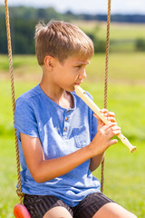 Boy sitting on swings and playing flute outdoors © vejaa
