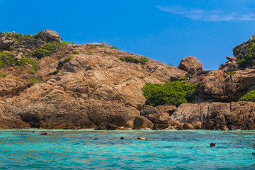 Fototapeta premium Lovely scenery with a blue sky, turquoise water & tourists snorkeling in front of the towering boulder rocks of Tokong Burung (Bird Island), a popular snorkeling spot near Perhentian Kecil, Malaysia.
