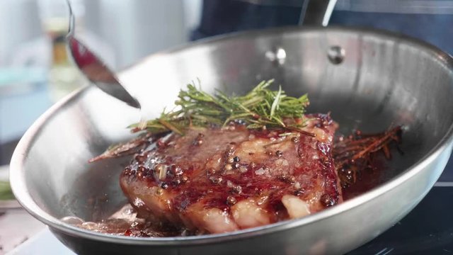 Meat steak is fried in oil and grease on frying pan, close-up in slow motion.