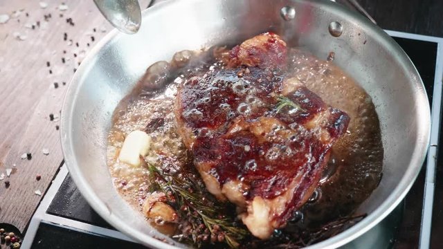 Meat steak is fried in oil and grease on frying pan, close-up in slow motion.