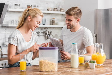 girlfriend using smartphone and boyfriend reading newspaper in kitchen