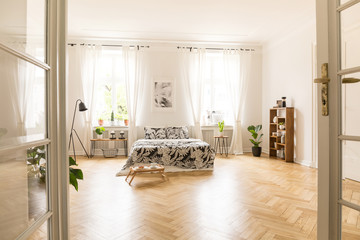 View through an open double door into a bedroom interior with wooden parquet, large windows and...