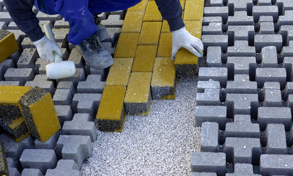 Paving stone worker is putting down pavers during a construction of a city street onto sheet nonwoven bedding sand and fitting them into place.