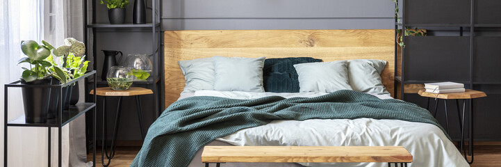 Green blanket on wooden bed in minimal grey bedroom interior with plants. Real photo