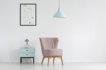 Cupboard, armchair, poster and lamp on a white, empty wall in a living room interior. Real photo. Place your graphic