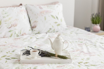Real photo with close-up of breakfast tray with tea cup, jug and lavender placed on double bed with floral bedclothes