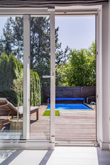 View through window on terrace with sunbed, swimming pool and trees. Real photo