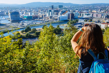Young woman standing on the view point of Oslo and enjoying the panorama of the city. Beautiful and soft sunlight. Norway.