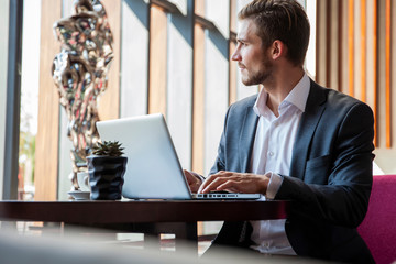 Young businessman working on laptop, sitting in hotel lobby waiting for someone.