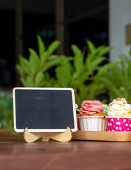 Naklejka na ściany i meble Colorful of homemade cupcake on wooden Tray with empty blackboard and copy space for your text.