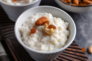 Delicious rice pudding with nuts and raisins in bowl on wooden board, closeup