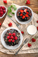 Plates with tasty chocolate pancakes, berries and milk on wooden table
