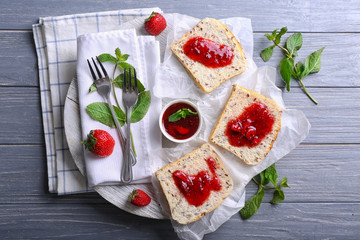 Board with slices of bread and delicious strawberry jam on wooden table