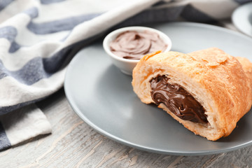 Tasty croissant with chocolate cream on plate, closeup