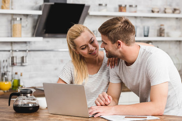 smiling couple working together with laptop in morning and looking at each other