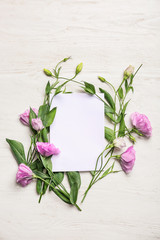 Beautiful eustoma flowers with blank card on white wooden background