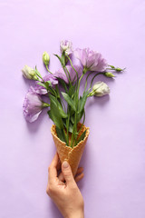 Woman holding waffle cone with beautiful eustoma flowers on color background